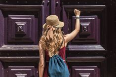 a woman wearing a hat standing in front of a purple door with her arms up