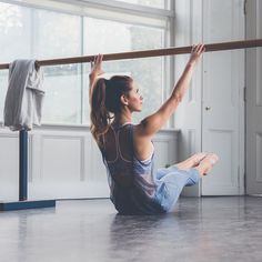 a woman sitting on the floor in front of a ballet pole and stretching her legs