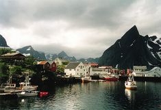 boats are docked in the water next to mountains and snow covered peaks on a cloudy day