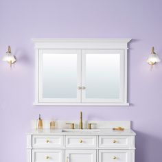 a white bathroom vanity with two mirrors above it and purple walls behind it, along with gold faucets