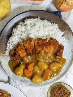 a plate with rice, meat and vegetables on it next to two bowls filled with gravy