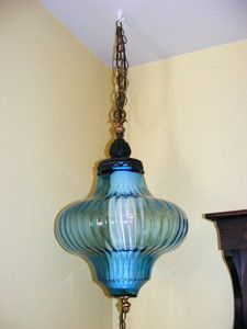 a blue glass lamp hanging from a chain on a wall next to a wooden table