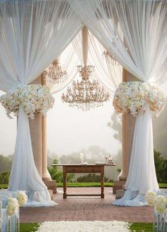 an open window with white drapes and flowers on the windowsill, in front of a chandelier