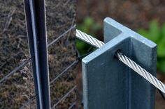 a close up of a metal fence post with two wires attached to it and grass in the background