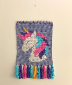 a crocheted unicorn is hanging on the wall with tassels around it