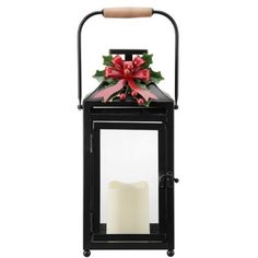 a black lantern with a red bow on it and a lit candle in front of it