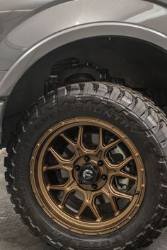 the front wheel and tire of a silver truck with gold rims on it's tires