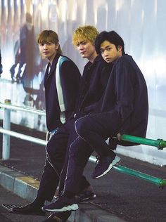 three young men sitting on the edge of a wall