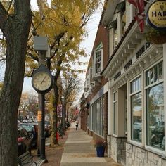 a clock sitting on the side of a building next to a sidewalk with cars parked in front of it