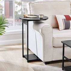 a white couch sitting next to a table on top of a wooden floor near a window