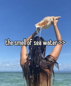 a woman standing in the water with her hands up to her head while holding a shell over her head