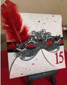 a white card with red feathers and a mask on it