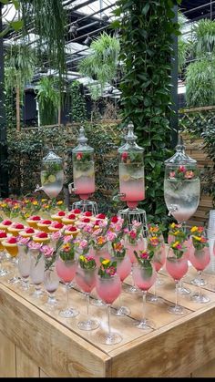 a table topped with lots of wine glasses filled with pink liquid and flowers in vases