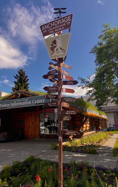 a pole with many signs on it in front of a building and some flowers around it