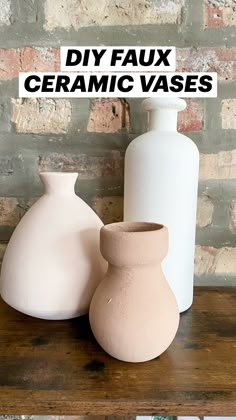 three white vases sitting on top of a wooden table next to a brick wall