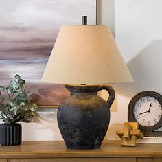 a lamp sitting on top of a wooden table next to a clock and potted plant