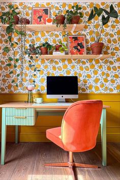 an orange chair sits in front of a desk with a computer monitor and plants on it