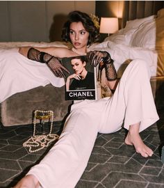 a woman is sitting on the bed with a book in her hand and she is holding a chandelier