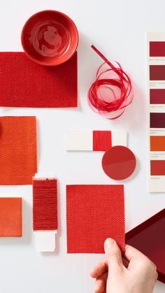 a person's hand is holding a piece of red paper next to some color swatches