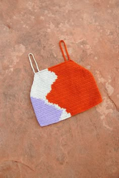 an orange, white and blue crochet bag sitting on top of a rock