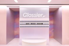 a white toilet sitting inside of a bathroom next to a wall mounted display sign with the word glossier on it