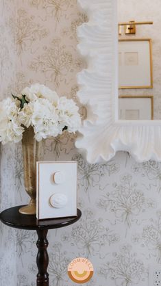 a vase with white flowers sitting on top of a small table next to a mirror