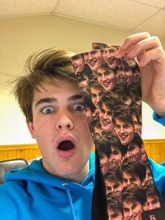 a young man holding up a tie with the faces of many people on it in front of his face