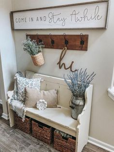 a white bench with some plants and baskets on top of it next to a sign that says come in and stay awhile