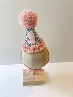 a pink pom - pom hat sitting on top of a wooden stand with a white wall in the background