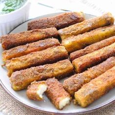 some fried food on a white plate with dipping sauce in the bowl next to it