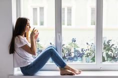 a woman sitting on a window sill drinking from a cup