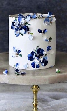 a white cake with blue flowers on it sitting on top of a gold plated stand