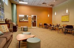 an empty room with chairs, tables and couches in the center is orange walls