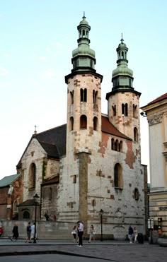 people are walking around in front of an old building with two towers and green spires