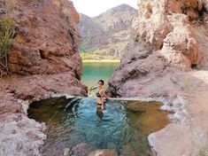 a woman wading in the water between two large rocks, with mountains in the background