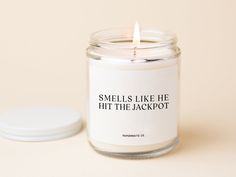 a candle with a quote on it sitting next to a small white container that says smells like he hit the jackpot