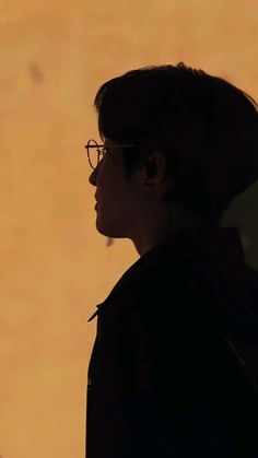 the silhouette of a woman wearing glasses against an orange sky