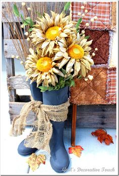 a blue boot with flowers in it sitting next to a pile of fall leaves and an old quilt