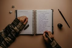 a person writing on a notebook with a pen