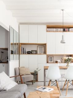 a living room filled with furniture next to a dining table and bookshelf on the wall