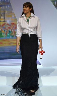 a woman in a white shirt and black skirt walking down a runway with a red purse