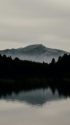 a lake with mountains in the background and fog on the water, as seen from across it