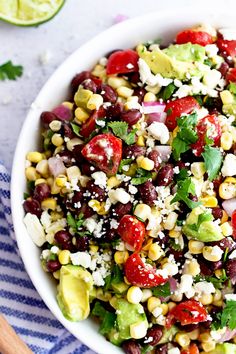 a white bowl filled with corn salad and garnished with cilantro, red onion, avocado wedges