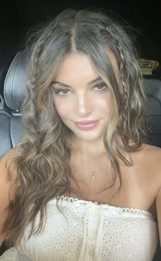 a woman sitting in the back seat of a car wearing a white top and long curly hair