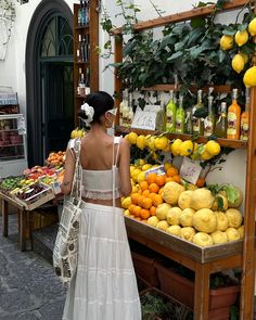 a woman in a white dress standing next to a fruit stand with lemons and oranges