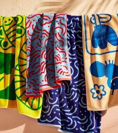 colorful towels hanging on a clothes line in front of a tan wall with blue and green designs