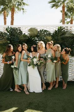 a group of women standing next to each other in front of palm trees and greenery