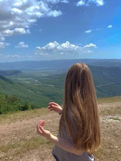 a woman standing on top of a hill with her hands out to the sky and mountains in the background