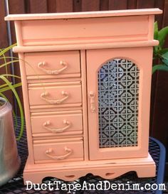 an old pink cabinet with metal doors and drawers on top of a table next to a potted plant