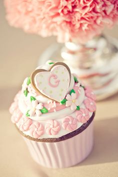 a cupcake decorated with pink flowers and a heart on top is sitting in front of a vase